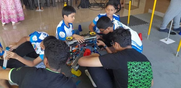Aniket kneels over his robot working on it with his team at a competition.