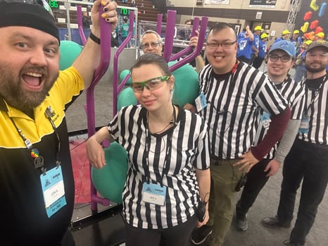 Jon stands in front of the Reefscape FRC game with a group of referees. 