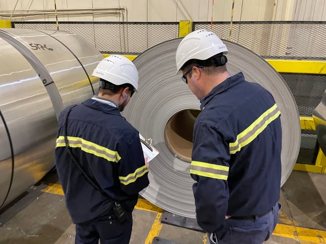 Michael and a colleague inspect a coil of aluminum to ensure it's quality.