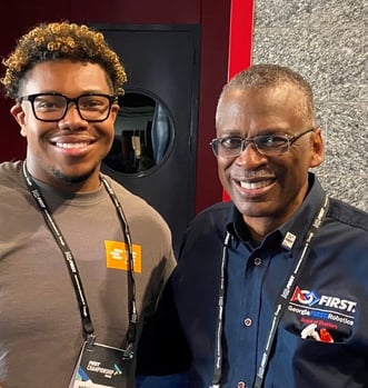 Nicholas and Lonnie Johnson pose together and smile. They are at a FIRST Robotics Competition.