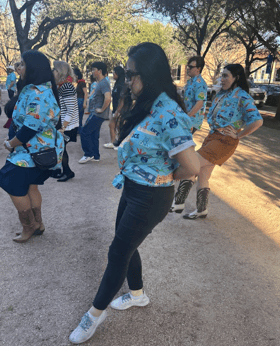 Sarah stands outside with a group of people in FIRST shirts doing a line dance.