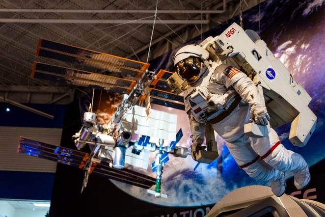A model and replica of an astronaut hangs in front of a satellite at the Space Center in Houston, Texas.