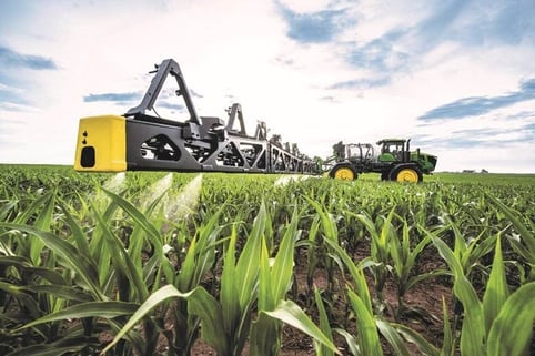 A yellow tractor stands in a green field with a blue, cloudy sky in the background