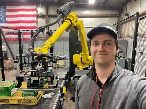 James smiles and poses for a selfie in front of a yellow robotic arm.