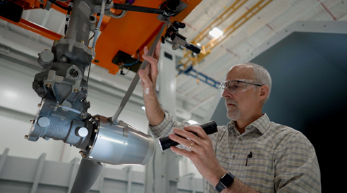 Ted uses a flashlight to inspect a robotic arm.