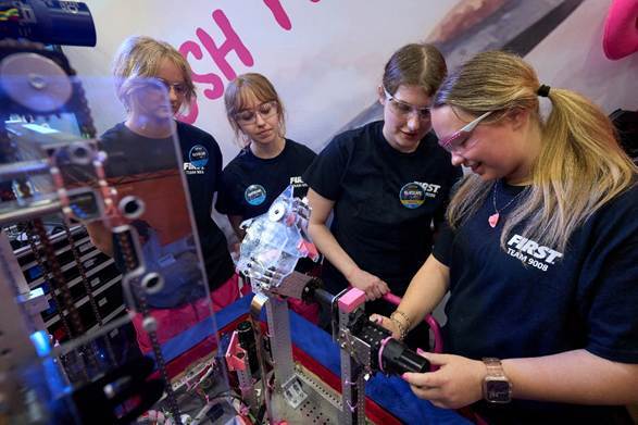 Four #girlsinSTEM stand around their robot working on it.