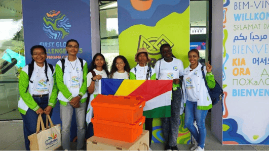 Team Seychelles poses in front of the FIRST Global Challenge 2025 sign. They are holding their country flag and smiling, posing with their gear.