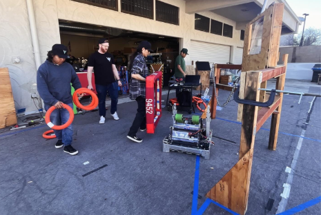 A group of LHS Stingers students holding various robot parts outside in a practice area.