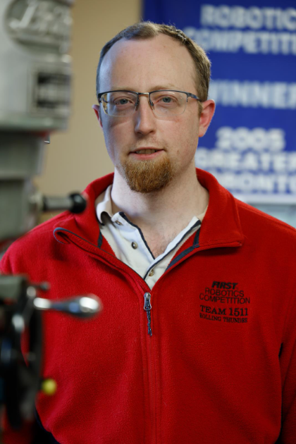 Ed smiles at the camera. The background is blurry, but an FRC banner can be seen. 