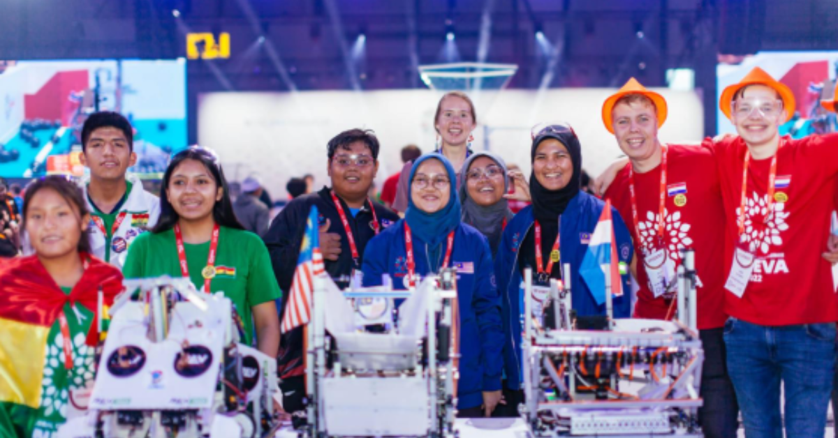 FIRST Global students stand with their robots smiling big and posing at a FIRST Global event. They are wearing colors and symbols from their countries.