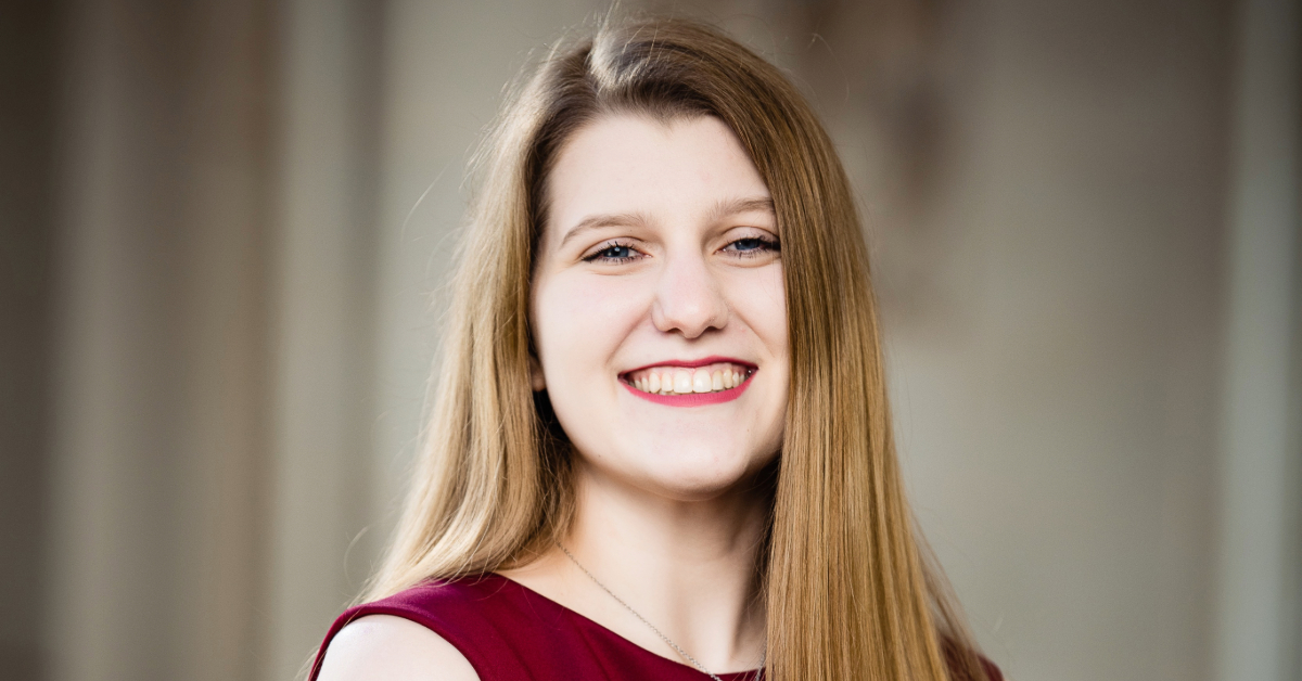 Lauren smiles wide for a professional headshot. She is wearing a simple red top.