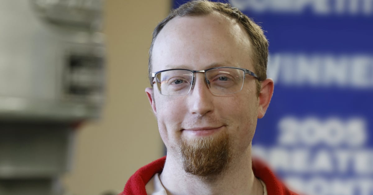 Ed smiles at the camera. The background is blurry, but an FRC banner can be seen. 