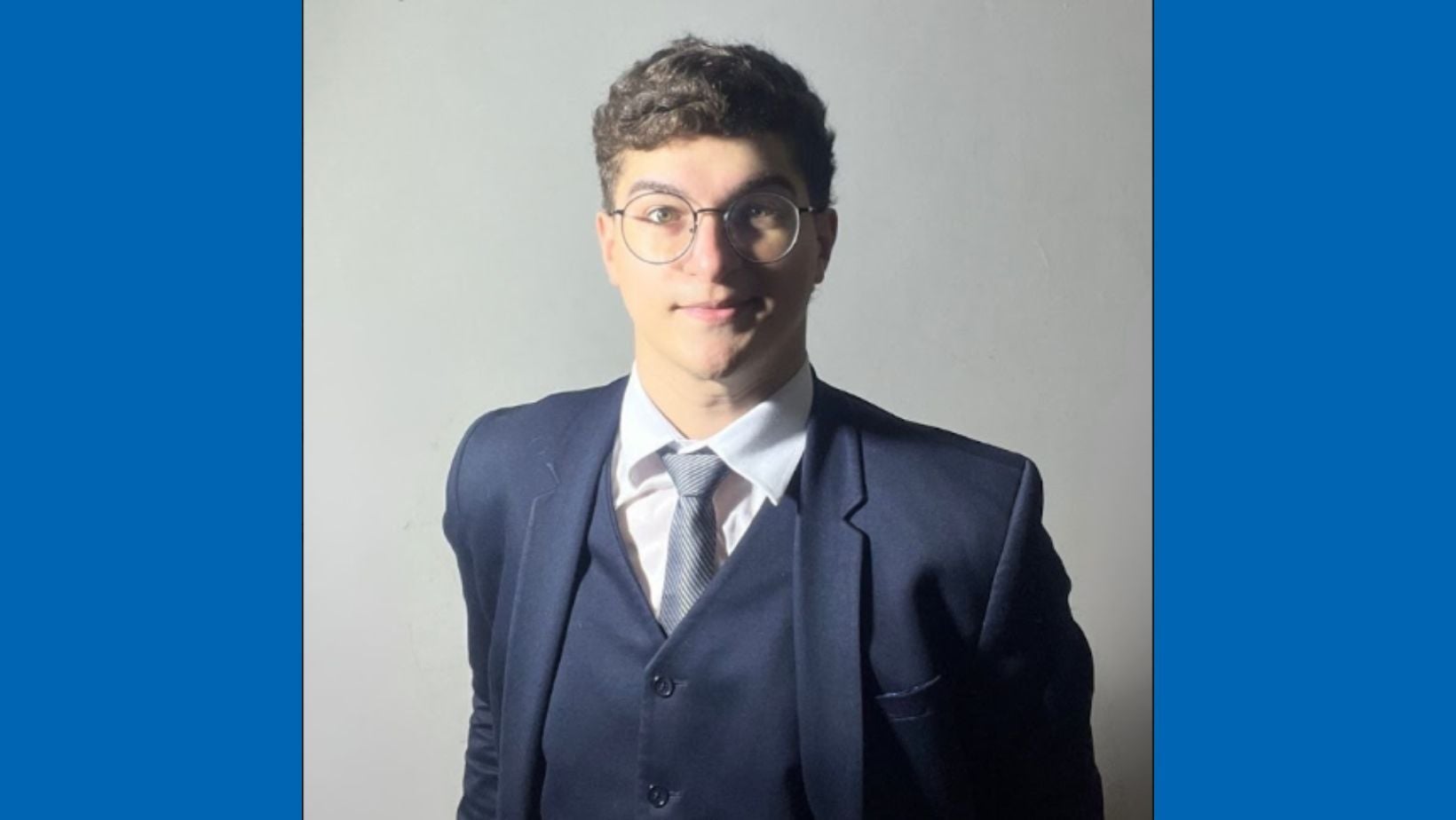 Joao stands in front of a neutral background, smiling for a professional headshot. He is wearing a navy blue suit.