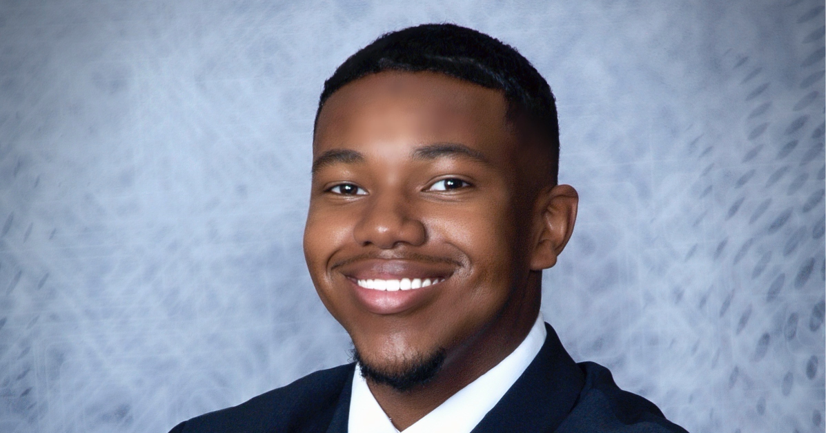 Nicholas stands in front of a blue background with a big smile on his face.