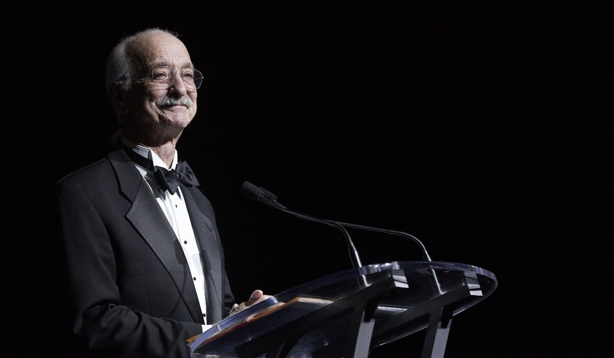 Woodie Flowers stands at a podium in a black tuxedo to present.