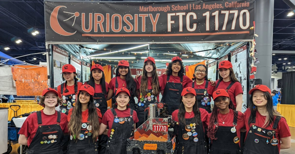 Team Curiosity smiles and poses with their robot in front of their pit at FIRST Championship.